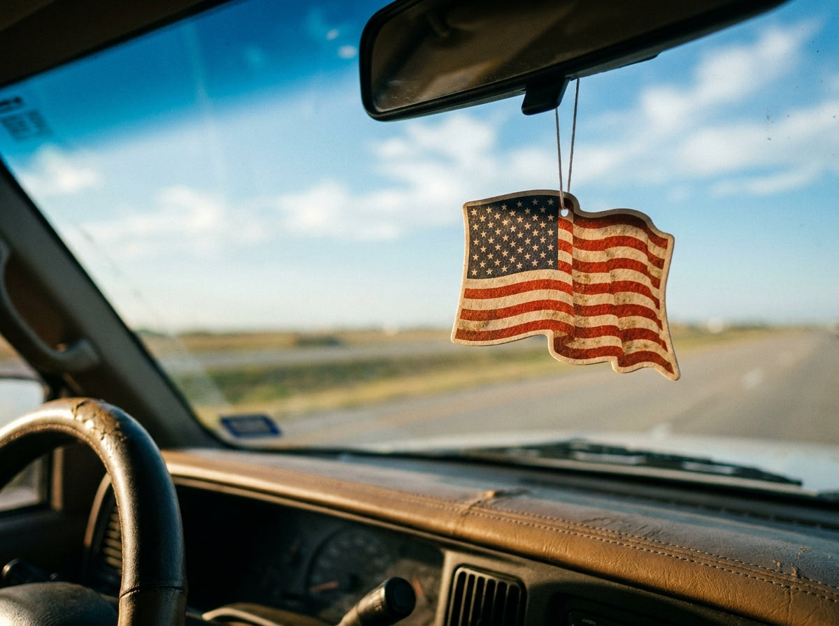 American flag air freshener hanging from a truck's rearview mirror with the open road behind